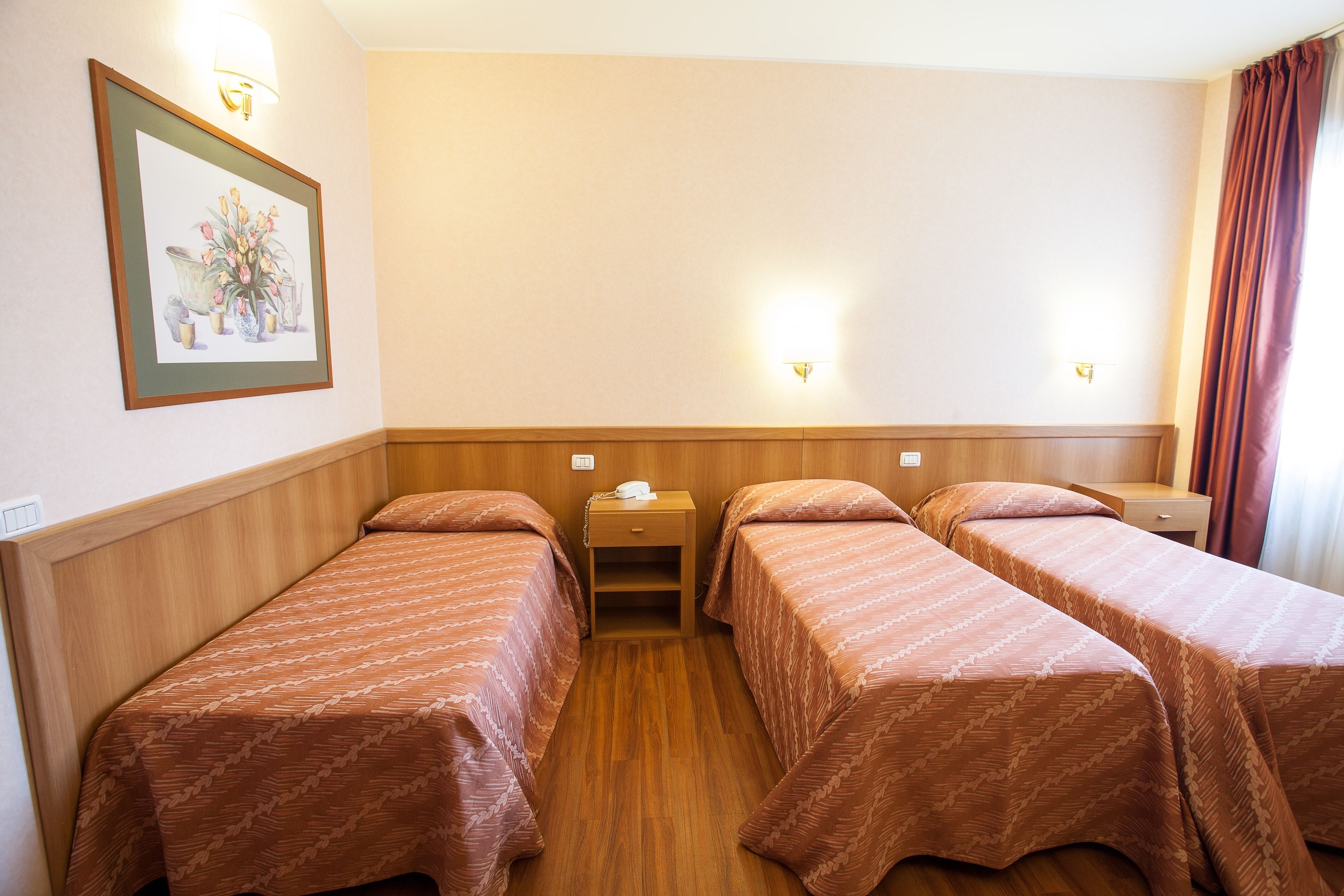 A hotel room with two single beds, wooden headboards, a nightstand with a lamp, and a framed picture on the wall.