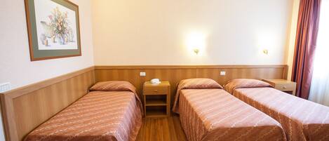 A hotel room with two single beds, wooden headboards, a nightstand with a lamp, and a framed picture on the wall.