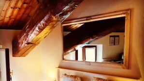 Une chambre avec un plafond en bois, un grand lit avec une literie blanche, une table de chevet avec une lampe et un miroir au-dessus du lit.