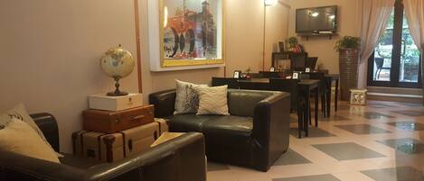 A living room with a black leather sofa, a globe, and suitcases. There is a painting on the wall, a television, and a dining area with a table and chairs.