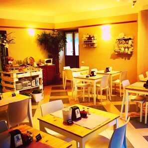 A dining area with multiple tables and chairs, a potted plant, and a microwave on a shelf.
