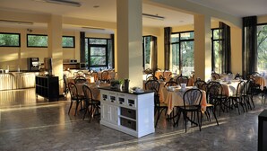 A spacious dining area with multiple tables and chairs, large windows, and a central island with a kitchen counter. - Hotel Beau Soleil (Cesenatico)