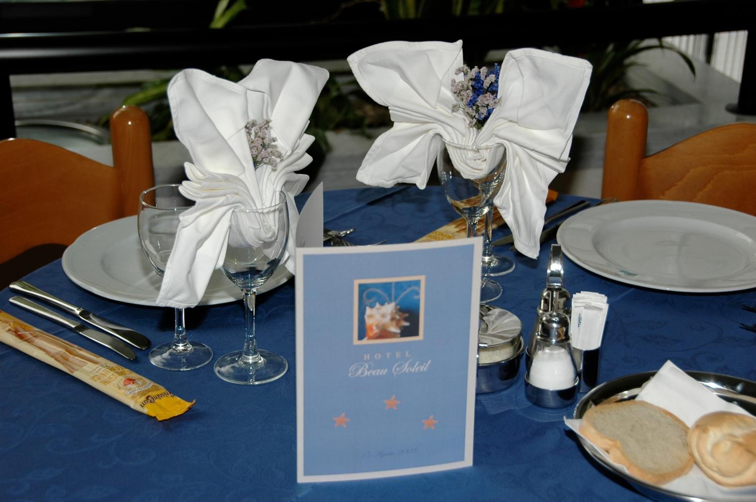 Ein gedeckter Tisch mit blauem Tischläufer, weißen Servietten und einer Speisekarte für das Hotel Beau Chalet.