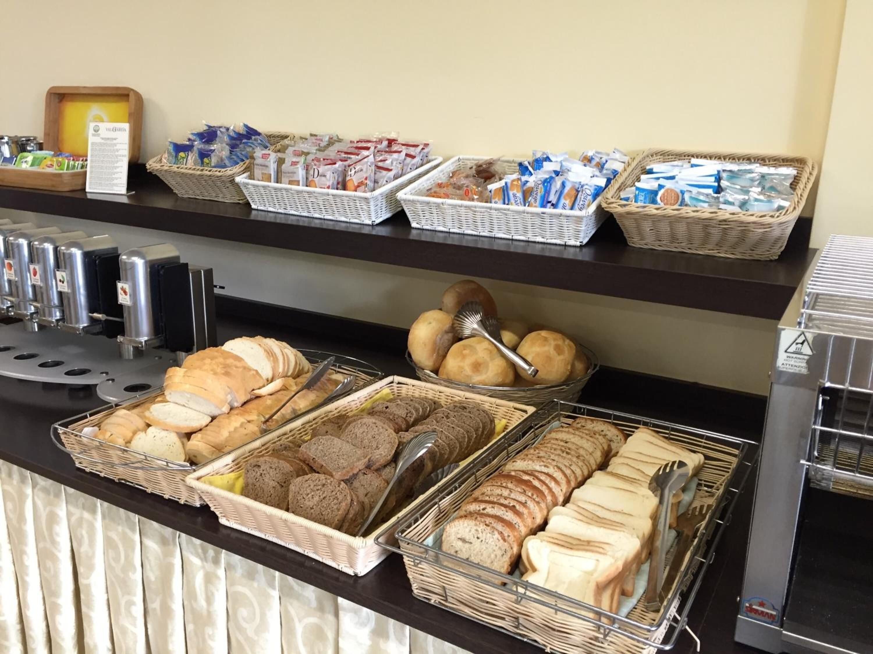 A breakfast buffet with various breads, pastries, and beverages.