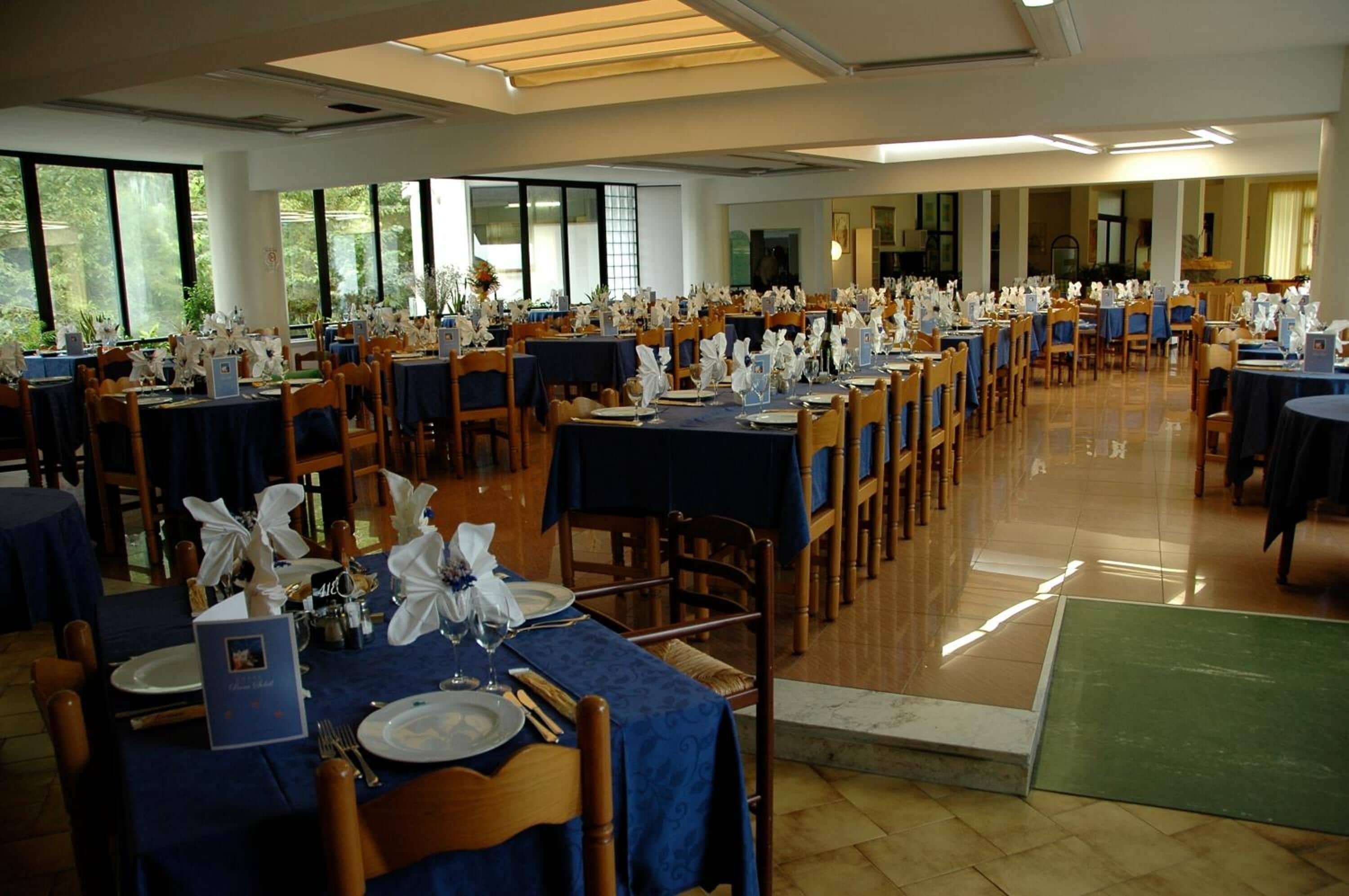 A large dining hall with multiple tables set for a formal event, featuring blue tablecloths and white table settings.