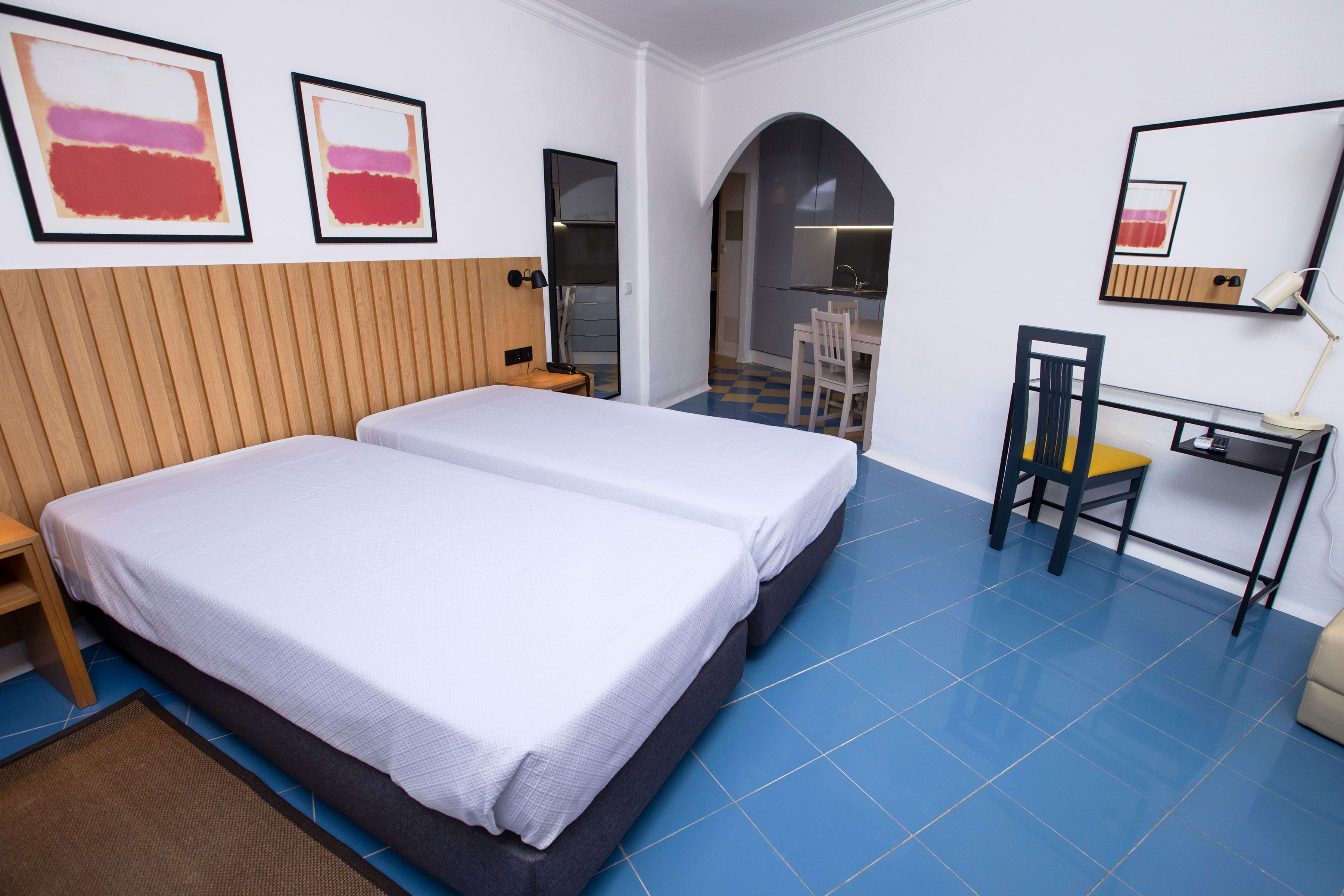 A hotel room with two beds, a desk, a chair, and artwork on the walls.