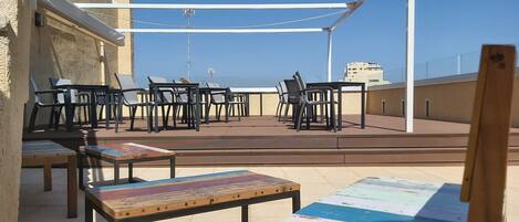 An outdoor terrace with tables and chairs, a white canopy, and a view of the sea.