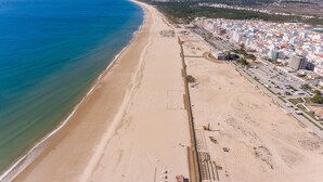An aerial view of a coastal city with a long sandy beach, adjacent residential buildings, and a clear blue sky. - Hotel Apartamentos Foz Atlântida (Vila Real Santo Antonio)