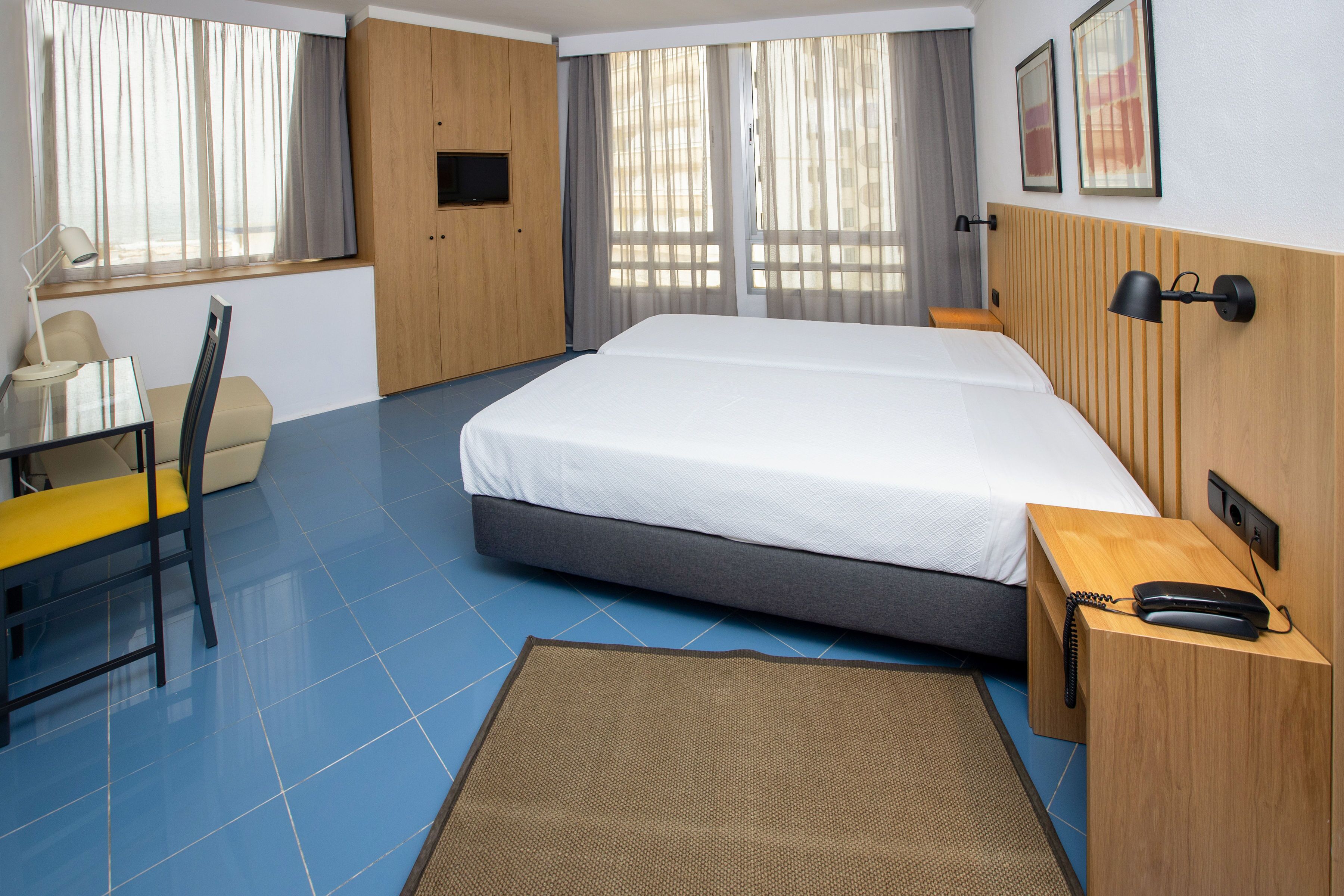 Una habitación de hotel con cama, escritorio, silla, televisor y teléfono.