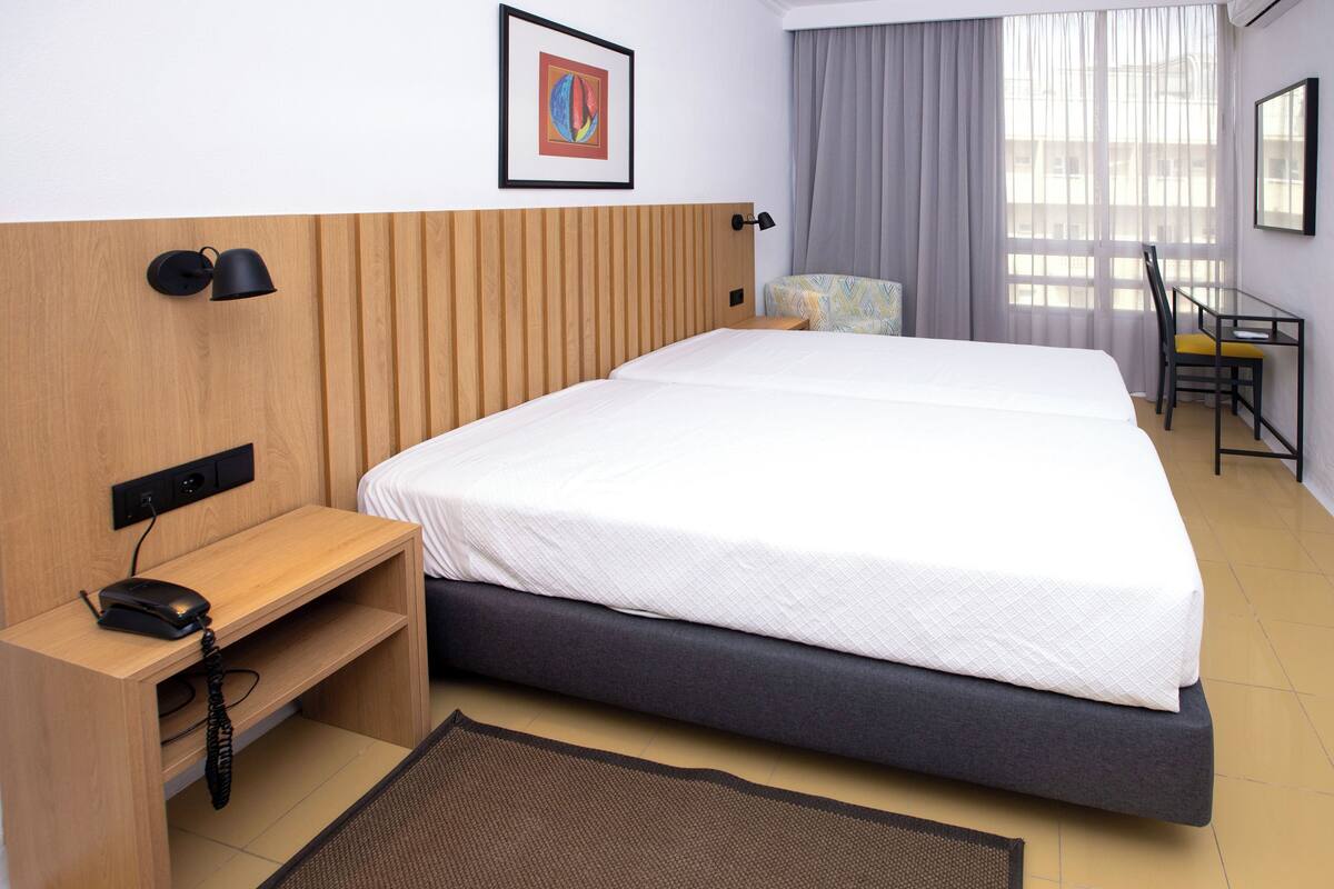 Une chambre d’hôtel avec un lit, un bureau, une chaise et une fenêtre avec des rideaux.