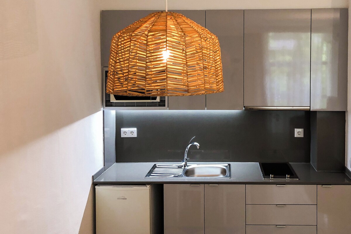 A modern kitchen with a stainless steel sink, a built-in oven, and a hanging woven light fixture.