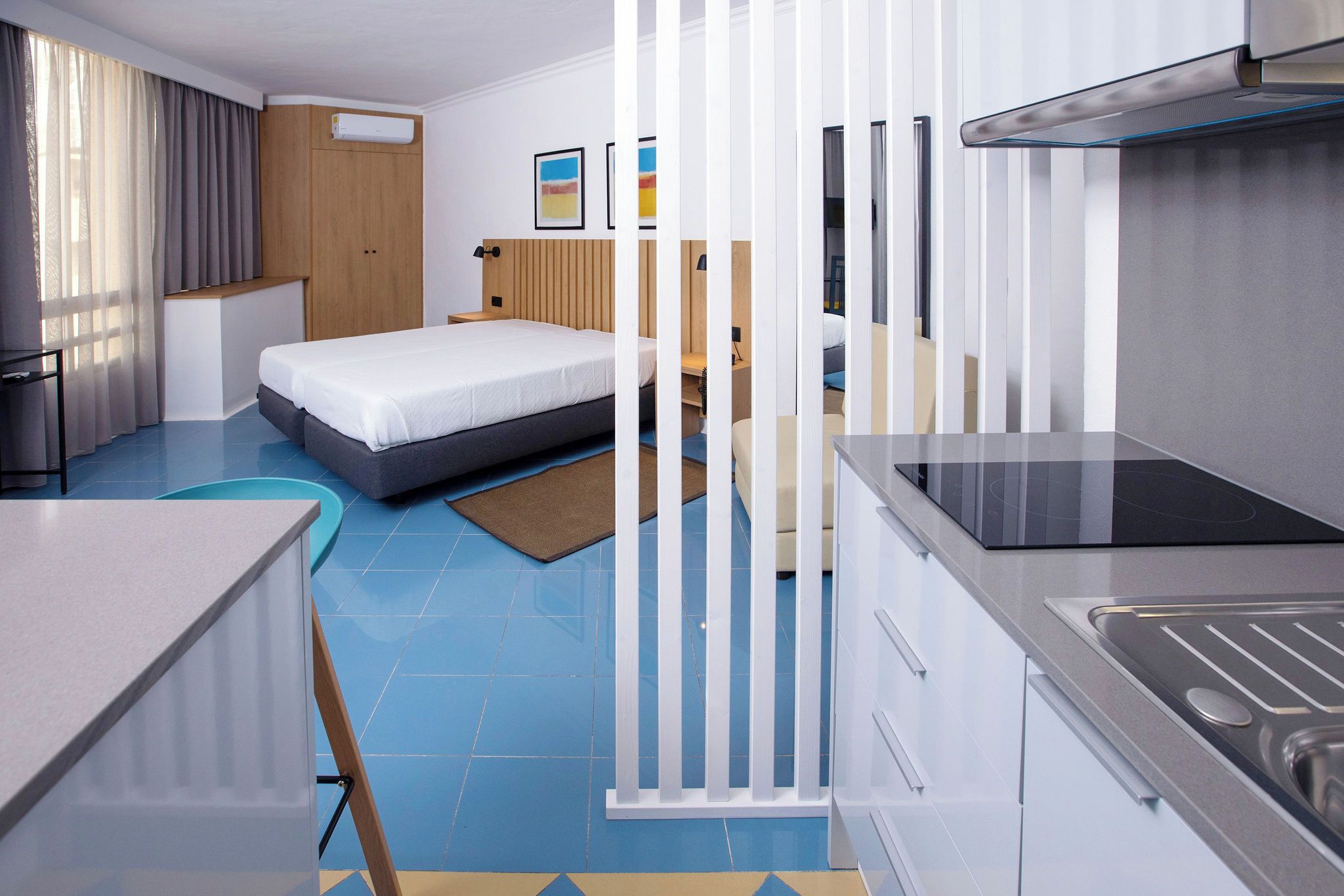 A modern hotel room with a bed, a kitchenette, and a bathroom.