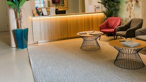 A reception area with a wooden reception desk, a large mirror, a red chair, a brown sofa, and a potted plant. - Hotel Apartamentos Foz Atlântida (Vila Real Santo Antonio)
