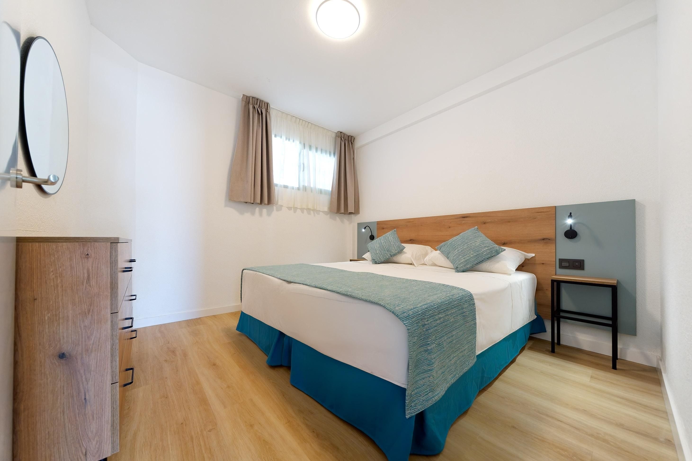Une chambre à coucher comprenant un lit, une tête de lit en bois, une table de chevet, un miroir et une armoire.