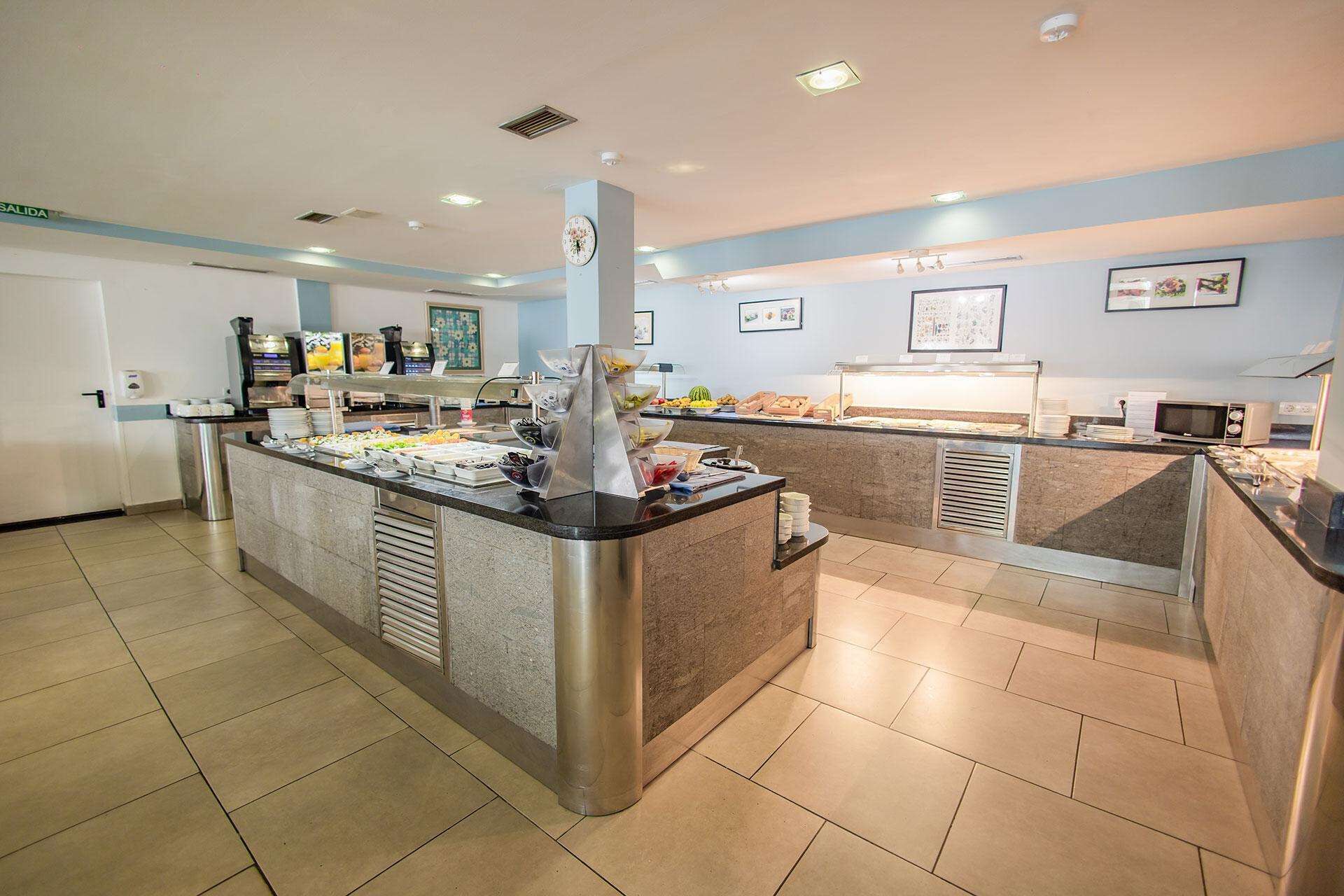 A buffet area with a variety of food items, a coffee machine, and a clock on the wall.