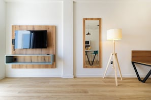 A modern living room with a mounted TV, wooden shelves, a standing lamp, and a mirrored wall. - Servatur Alameda de Jandía (Pajara)