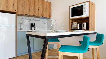 Cocina moderna con armarios de madera, un refrigerador blanco, microondas integrado y una mesa de comedor con sillas color turquesa.