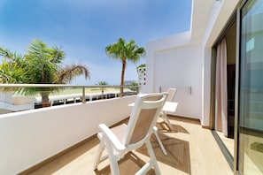 A balcony with white chairs and a palm tree, overlooking a beach. - Servatur Alameda de Jandía (Pajara)
