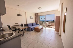 A modern hotel room with a dining area, a sofa, a coffee table, and a balcony with a view of the sea. - Servatur Alameda de Jandía (Pajara)
