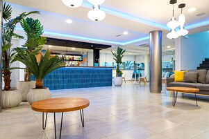 A modern lobby with a bar area, seating, and potted plants.