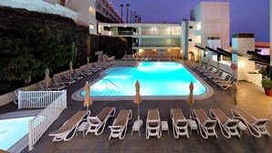 A pool area with sun loungers and umbrellas, surrounded by a building with a modern design and a view of palm trees. - Servatur Alameda de Jandía (Pajara)