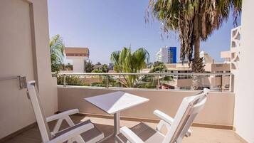 A balcony with two white chairs and a table, overlooking a cityscape with palm trees and buildings.