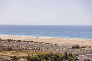 A beach with a sandy shore, sparse vegetation, and a clear view of the ocean. - Servatur Alameda de Jandía (Pajara)