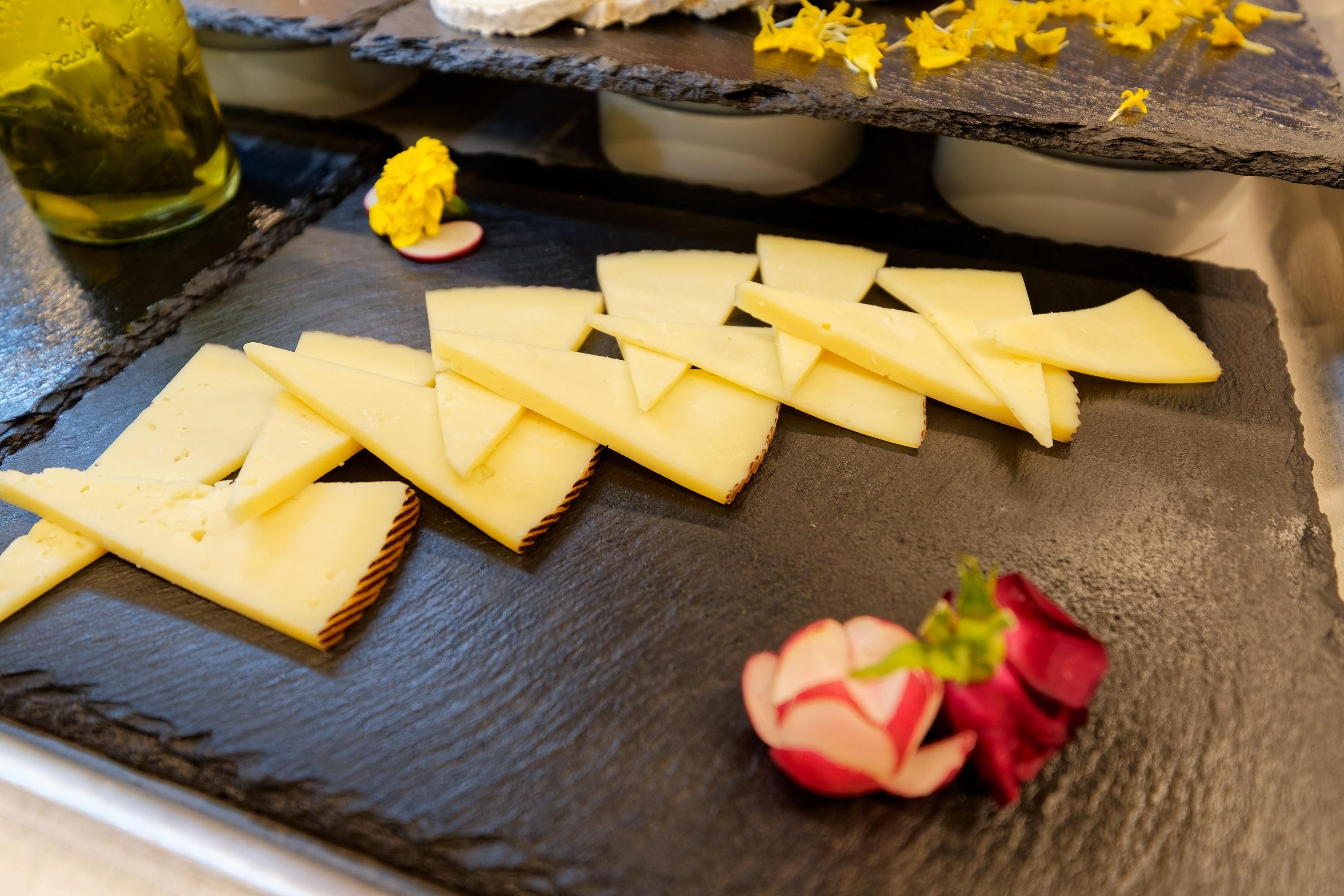 A slate serving board with cheese slices and a flower decoration.