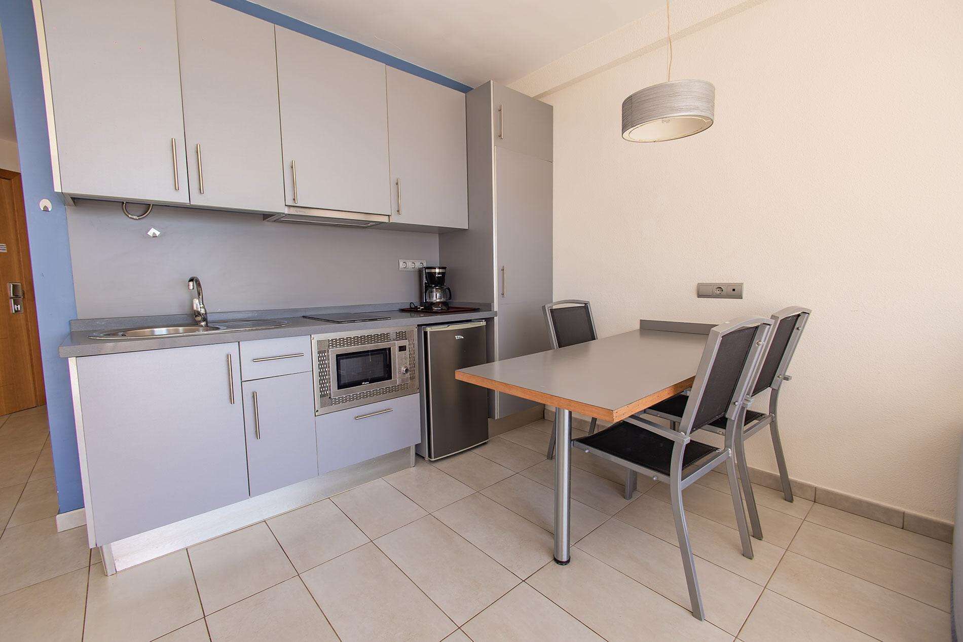 A compact kitchen with a built-in oven, a coffee maker, and a dining table with chairs.