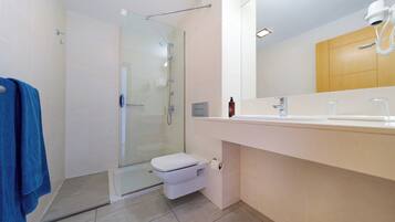 A modern bathroom with a glass shower enclosure, a white toilet, and a large mirror above a white sink.