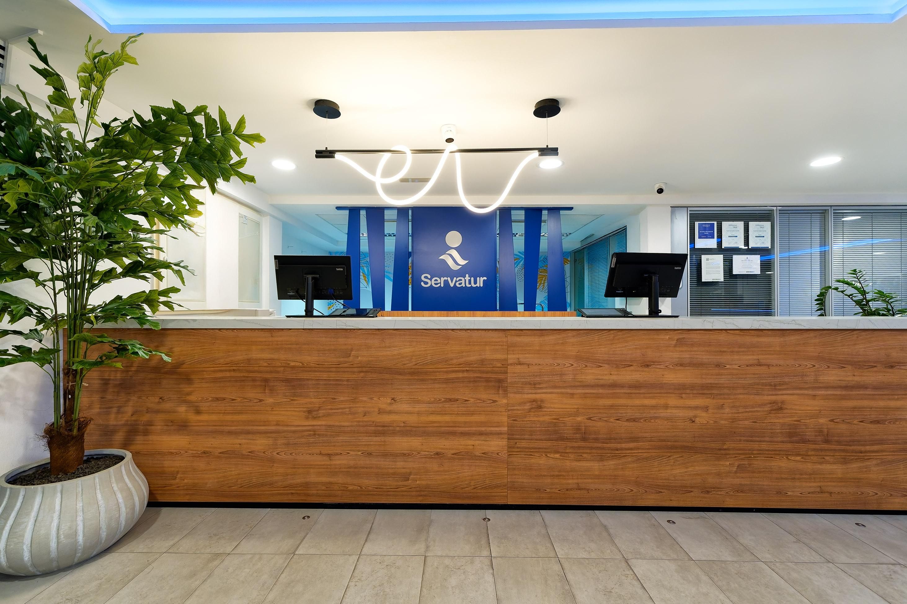 A reception desk with a logo, two monitors, and a potted plant.
