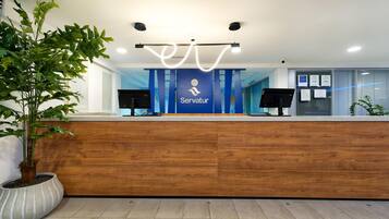 A reception desk with a logo, two monitors, and a potted plant.