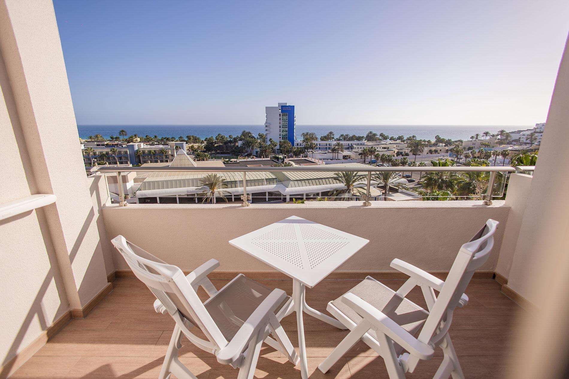 Un balcón con mesa y sillas, con vista a la playa y al paisaje urbano.