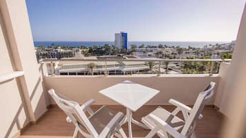 Un balcón con mesa y sillas, con vista a la playa y al paisaje urbano.