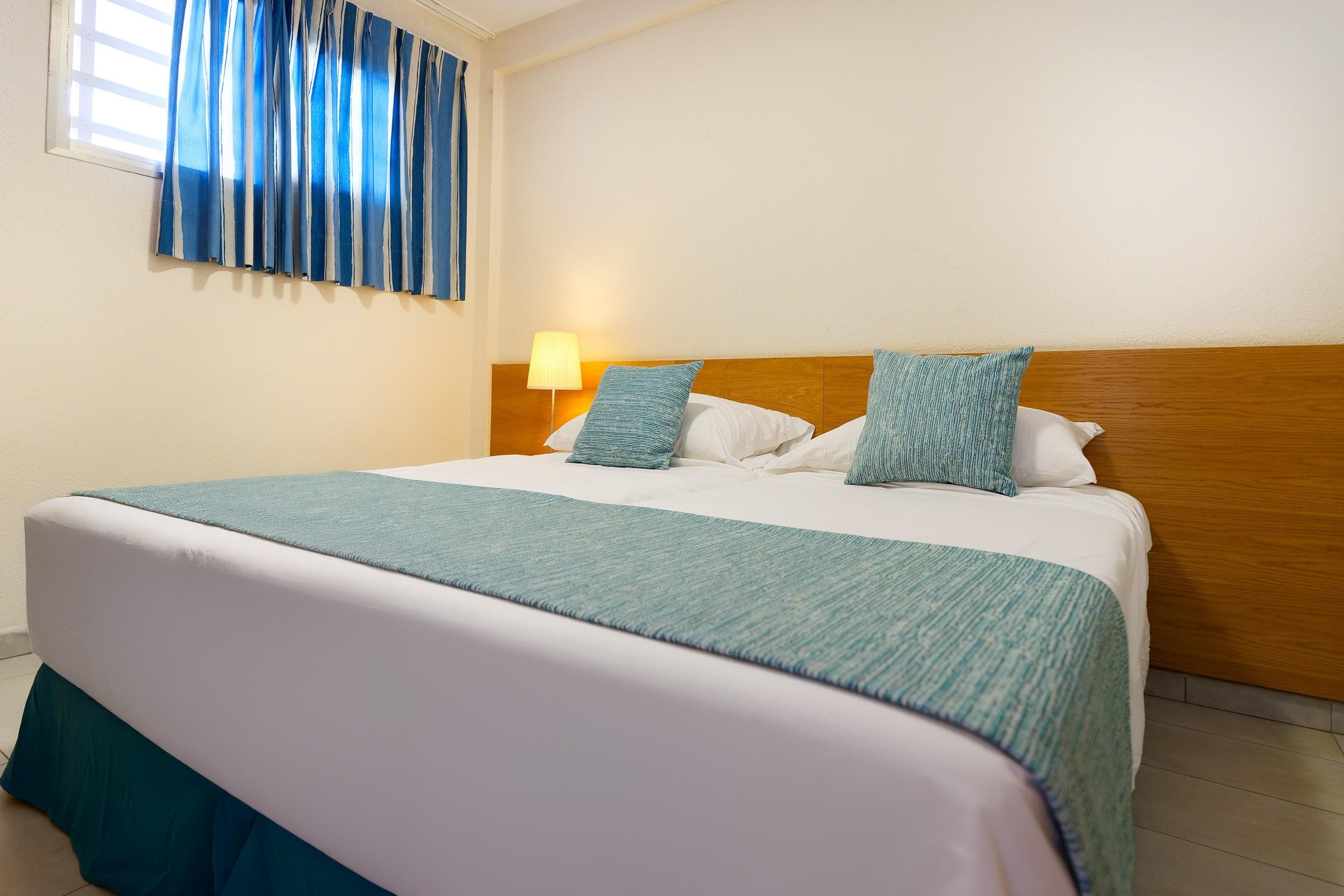 Ein Hotelzimmer mit einem großen Bett, einem Holzkopfteil, einem Nachttisch mit Lampe und einem Fenster mit blauen Vorhängen.