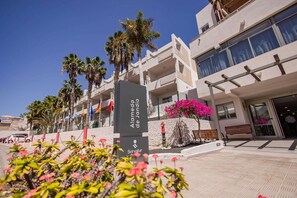 A hotel entrance with palm trees, a flower bed, and a sign indicating 'Servatür Hotel'. - Servatur Alameda de Jandía (Pajara)