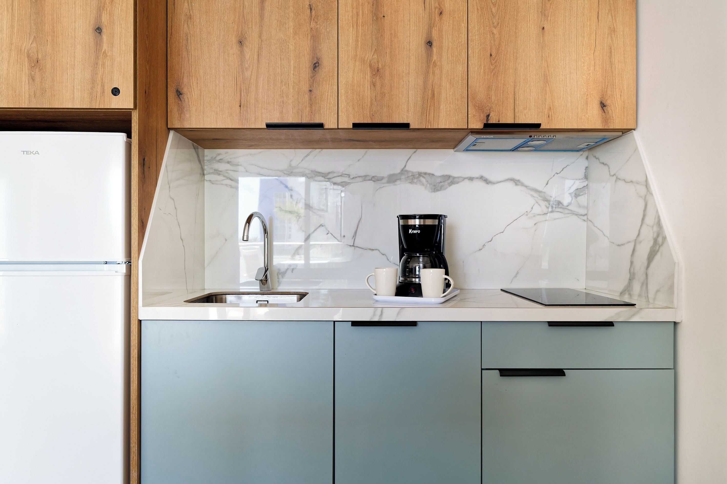 A kitchen with a white marble backsplash, a coffee maker, and a sink.