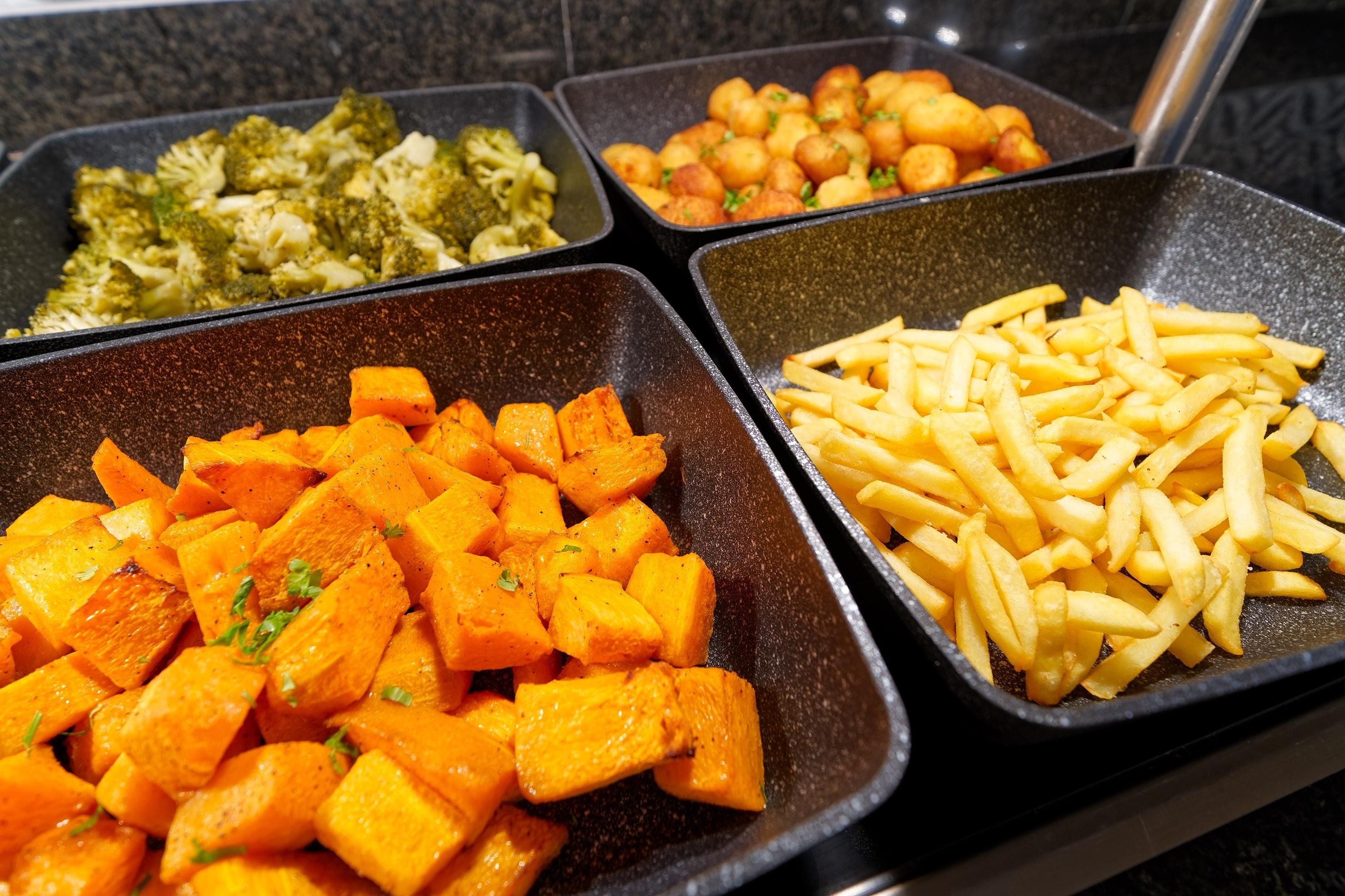 Een buffet met diverse gerechten, zoals geroosterde wortelen, friet en broccoli.