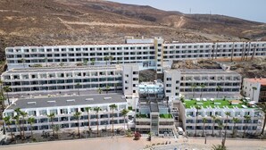 A modern hotel complex with multiple floors, a central courtyard with a pool, and a mountainous backdrop. - Servatur Alameda de Jandía (Pajara)