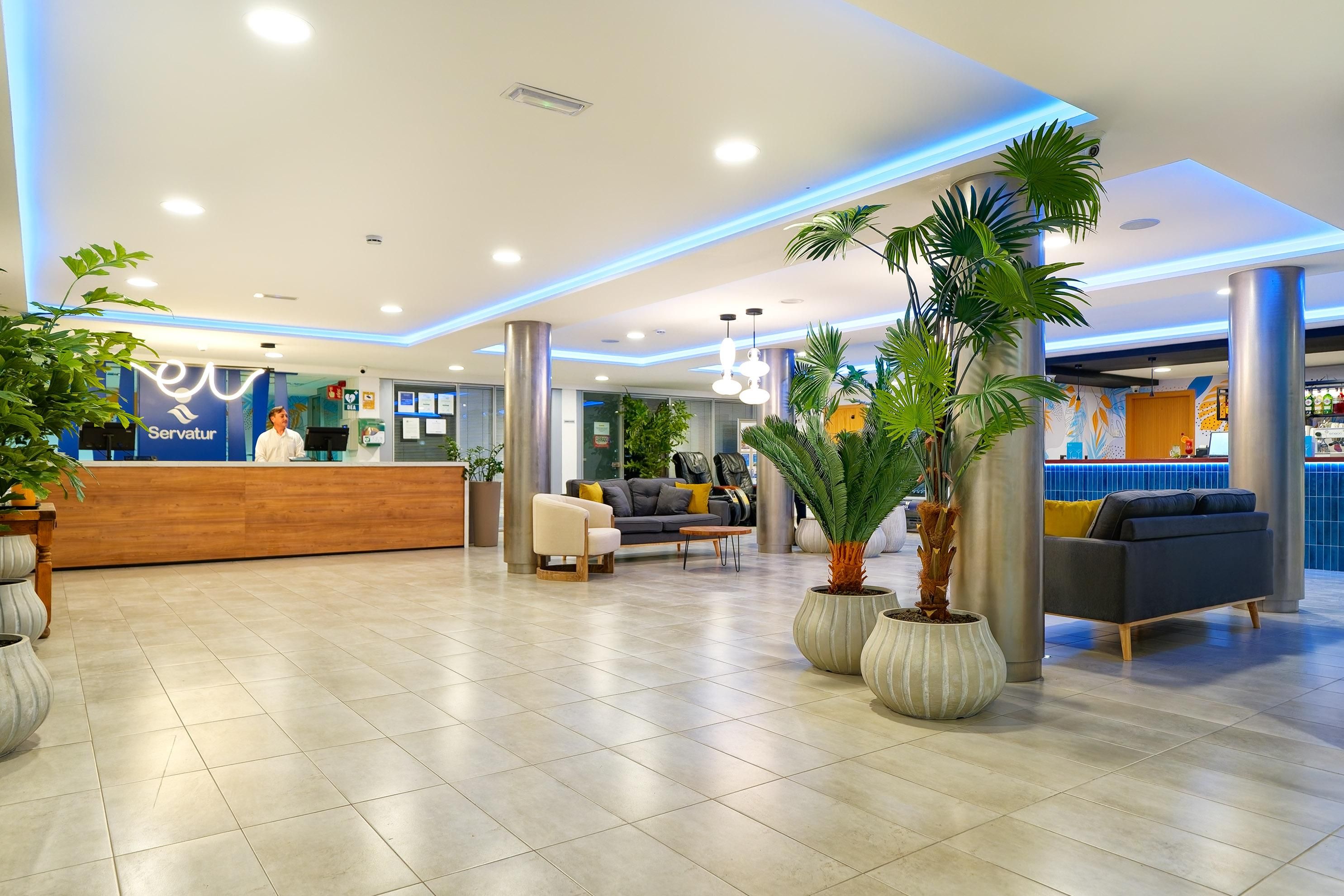 Zona d'entrada d'un hotel amb taulell de recepció, zona de seients i plantes en testos.