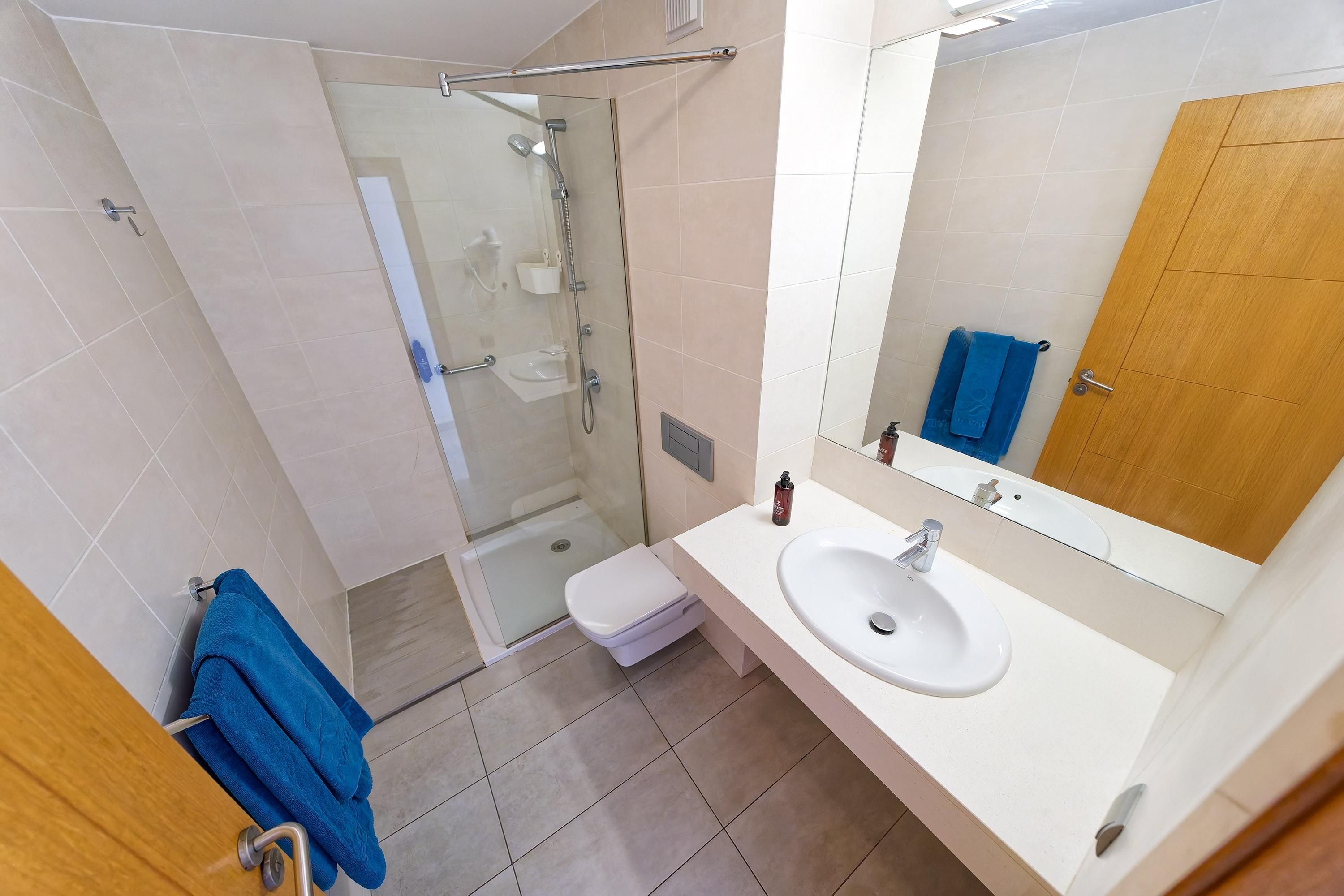 A bathroom with a glass-enclosed shower, a white sink, and a wooden door.