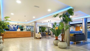 A modern hotel lobby with a reception desk, seating area, and potted plants. - Servatur Alameda de Jandía (Pajara)