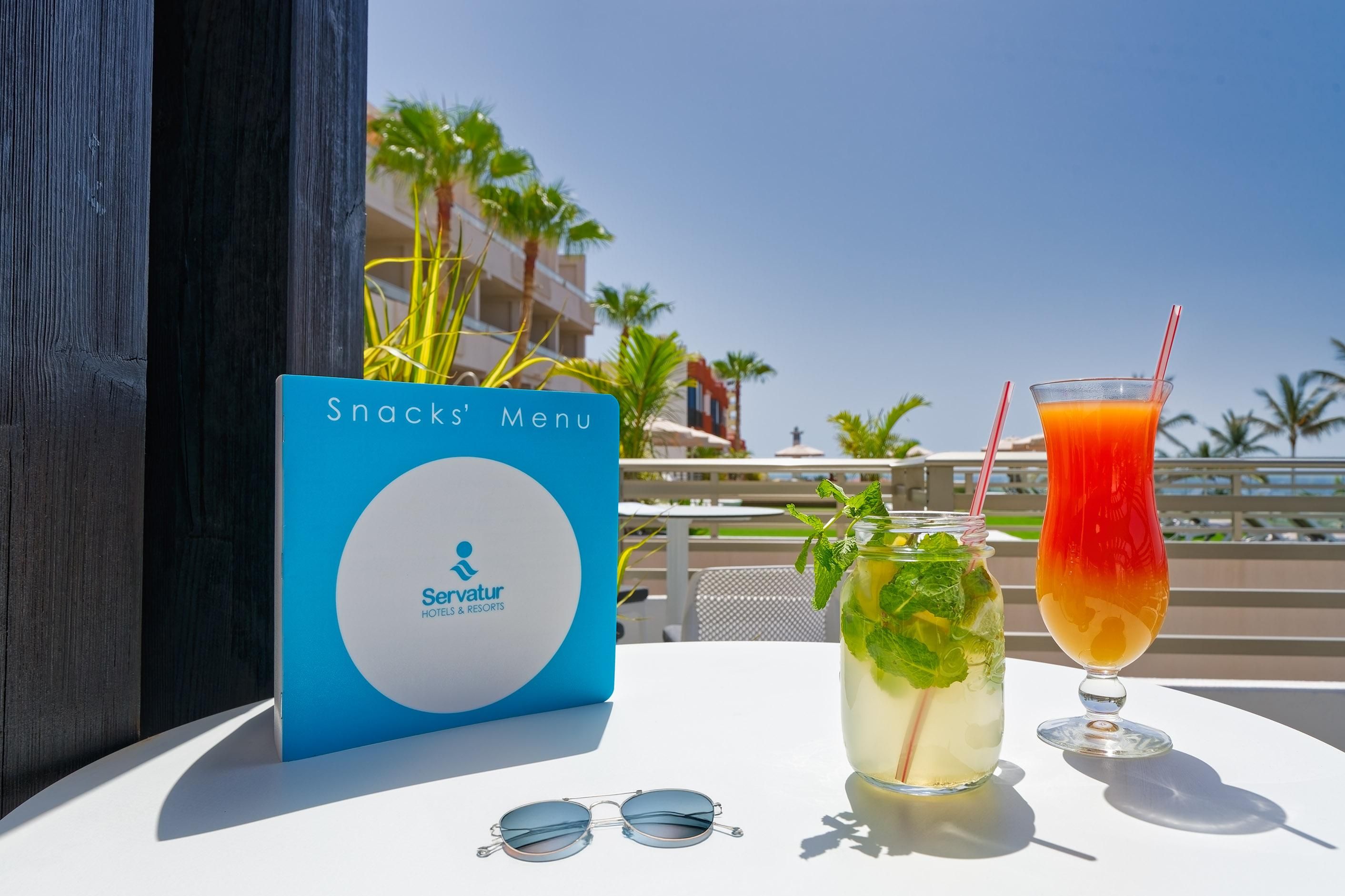 A table with a menu sign, a glass of orange juice, a glass of iced tea, and a pair of sunglasses.