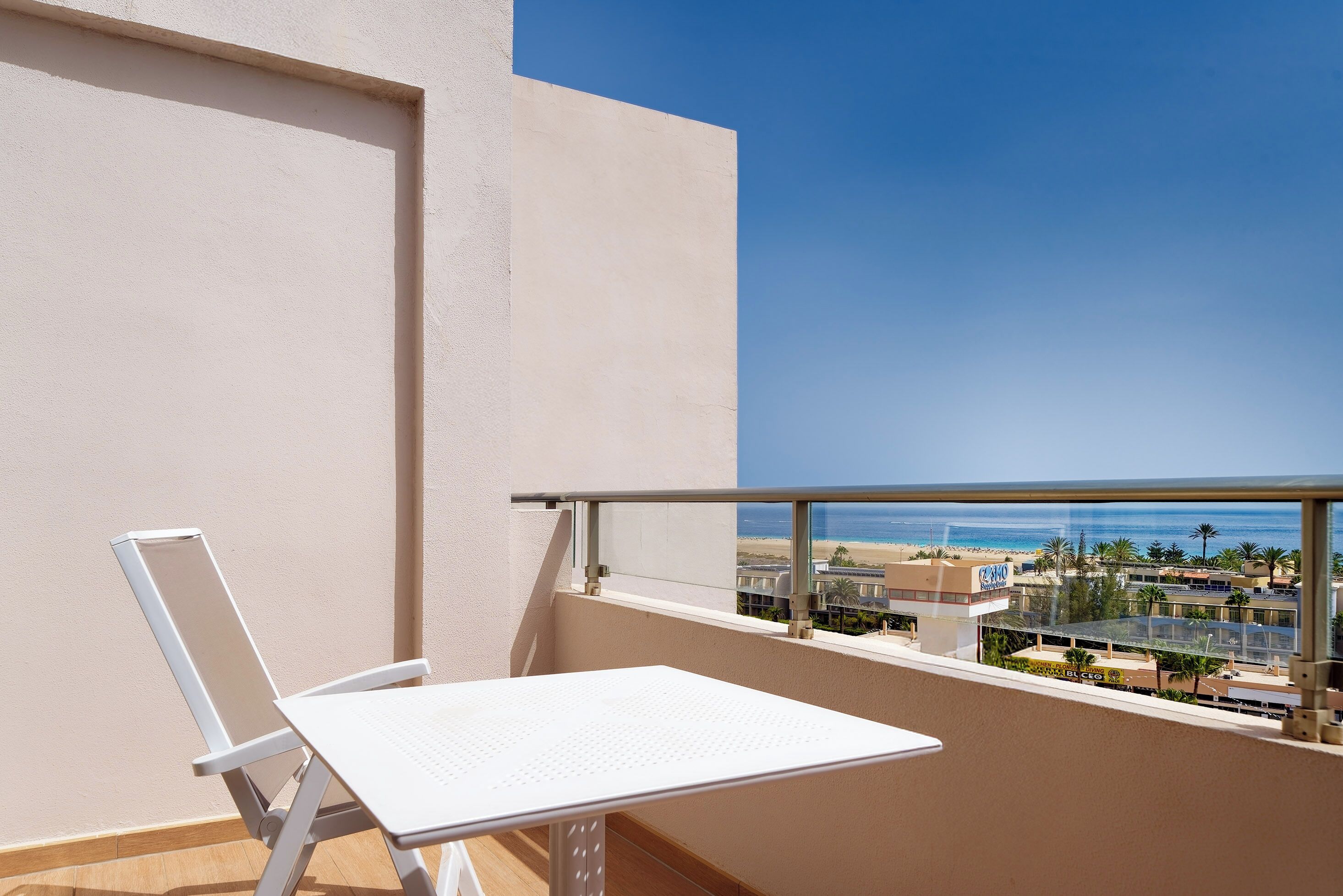 A balcony with a white table and chair, offering a view of a beach and cityscape.
