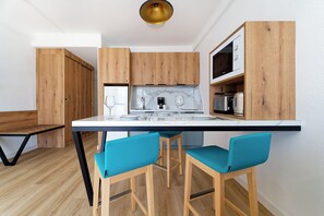 A modern kitchen with wooden cabinets, a white countertop, and two blue bar stools. - Servatur Alameda de Jandía (Pajara)