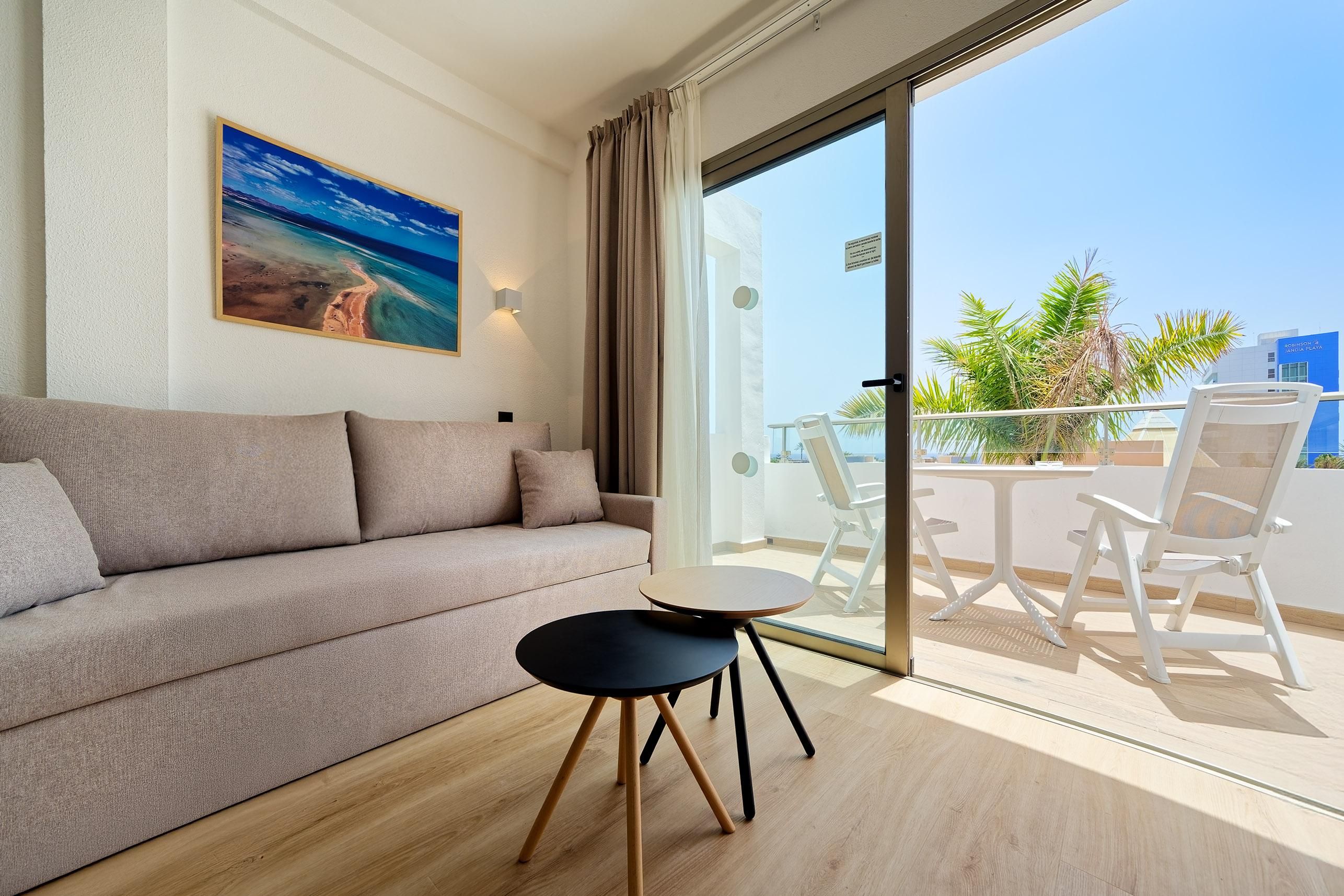 A modern living room with a sofa, a small round table, and a balcony with chairs and a view of the city.