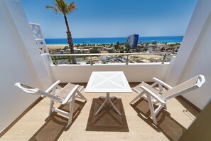Un balcón con mesa y sillas blancas, con vista a una playa y al océano.