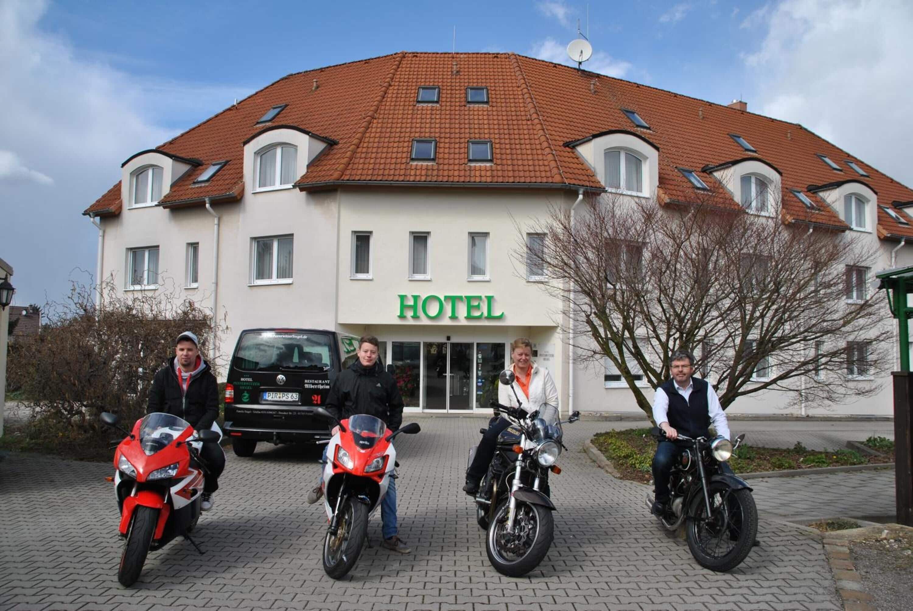 A hotel with a red-tiled roof, a sign reading "HOTEL", and three people on motorcycles in front.
