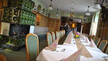 Restaurante com uma longa mesa de jantar posta para uma refeição, cadeiras de madeira e um bar com copos verdes.