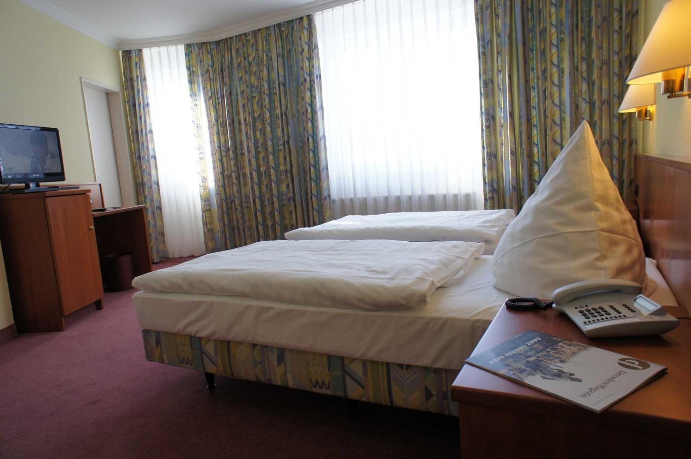 A hotel room with two beds, a desk with a lamp, a telephone, and a television.